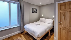Een slaapkamer met een bed, een raam, een deur en een schilderij aan de muur.