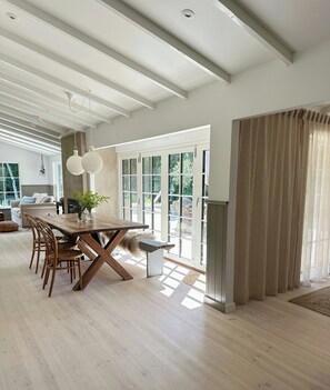 A spacious dining area with a wooden table and chairs, a large window with a view of the outdoors, and a modern ceiling design. - Cozy beach house with garden and vintage finds (Tisvilde)