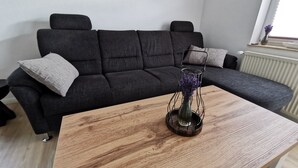 A modern living room with a dark grey sofa, a wooden coffee table, and a vase with purple flowers.