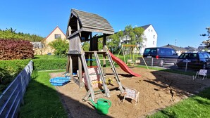 A playground with a wooden slide and climbing structures, surrounded by a fenced area.
