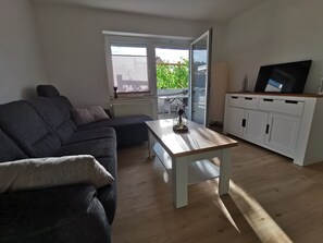 Un salon comprenant un canapé, une table basse, un téléviseur et une porte-fenêtre coulissante donnant sur une terrasse.