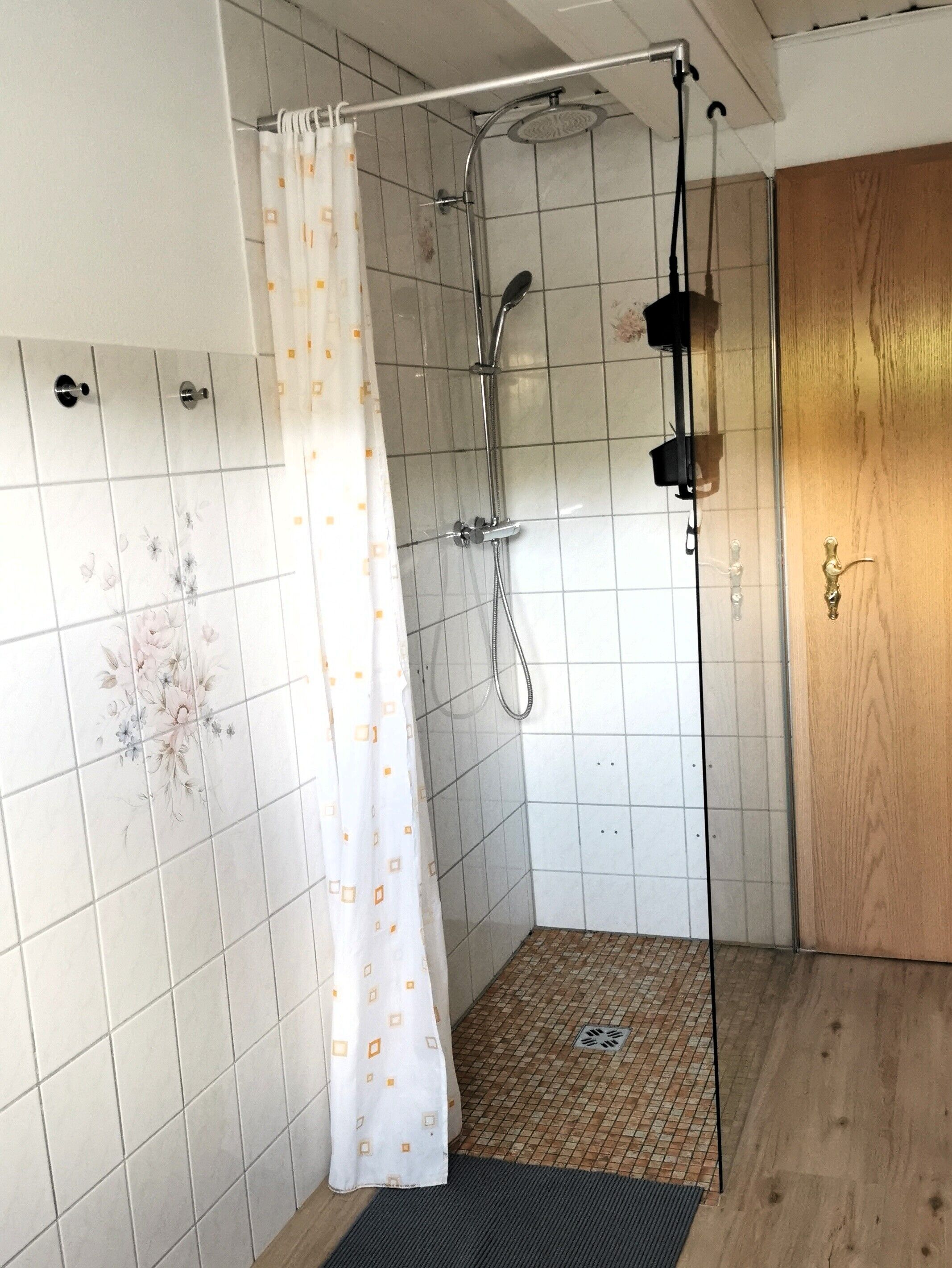 Ein Duschbereich mit Duschkopf, Vorhang und gefliesten Wänden.