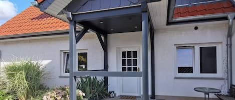A residential building with a covered porch, a front door, and a small outdoor seating area.