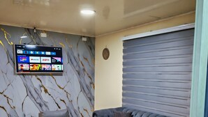 A modern living room with a sofa, armchair, ottoman, and a flat-screen TV mounted on the wall displaying various channels. - LPW STORE SARIE BAY No. 01 (san Andrés islas, colombia)