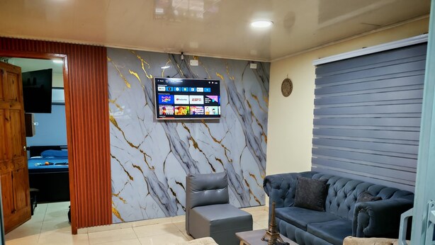 A modern living room with a marble-patterned wall, a television mounted above a sofa, and a wooden door leading to another room. - LPW STORE SARIE BAY No. 01 (san Andrés islas, colombia)