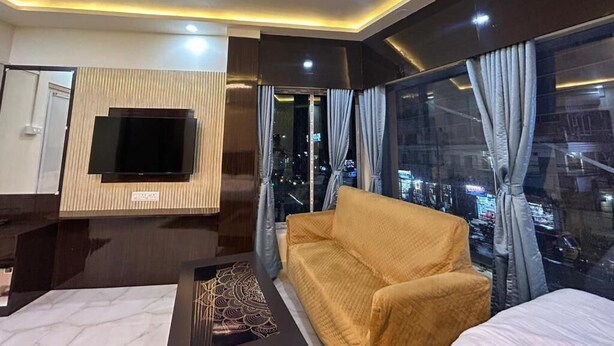 Una habitación de hotel moderna con un televisor de pantalla plana grande montado en la pared, un sofá, una cama y un ventanal con vistas a la ciudad.