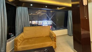 Una habitación con sofá, televisor, aparador de madera y ventana con cortinas.