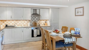 Een moderne keuken met witte kasten, een inbouwoven en een eethoek met een houten tafel gedekt voor twee personen.