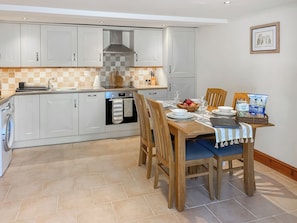 A modern kitchen with white cabinets, a built-in oven, and a dining area with a wooden table set for two.