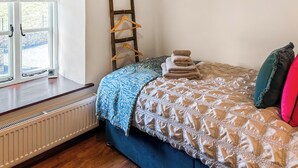 Een slaapkamer met een bed, een radiator, een raam met uitzicht en een houten kledingrek.