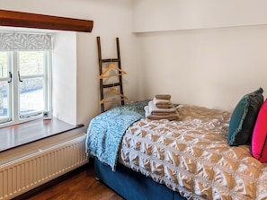Un dormitorio con cama, un radiador, una ventana con vistas y un perchero de madera.