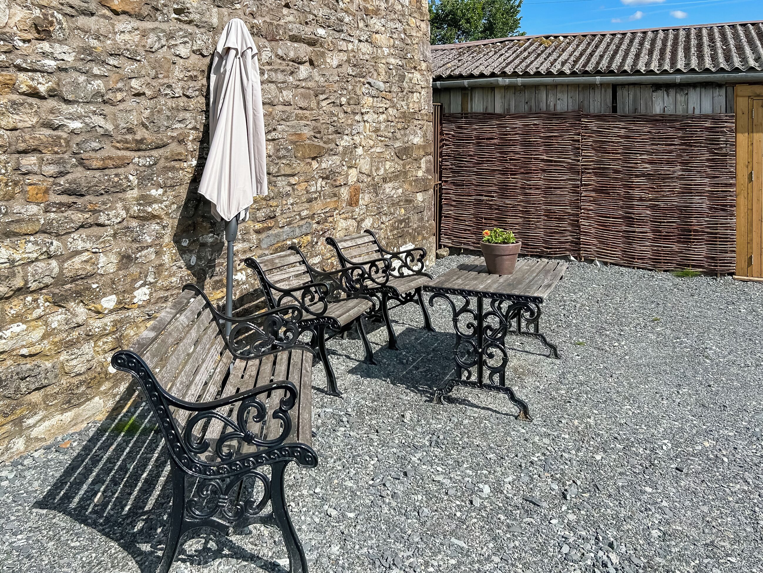 An outdoor seating area with stone walls, a wooden table, and metal chairs.