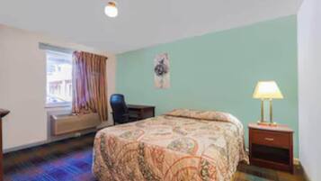 Une chambre d’hôtel avec un lit, une chaise, un bureau, une lampe et une fenêtre avec des rideaux.