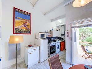 A compact kitchen with a microwave, oven, and washing machine, a small white cabinet, and a dining area with a table and chairs. - L'île des Marinas by Interhome (Cap d'Agde)