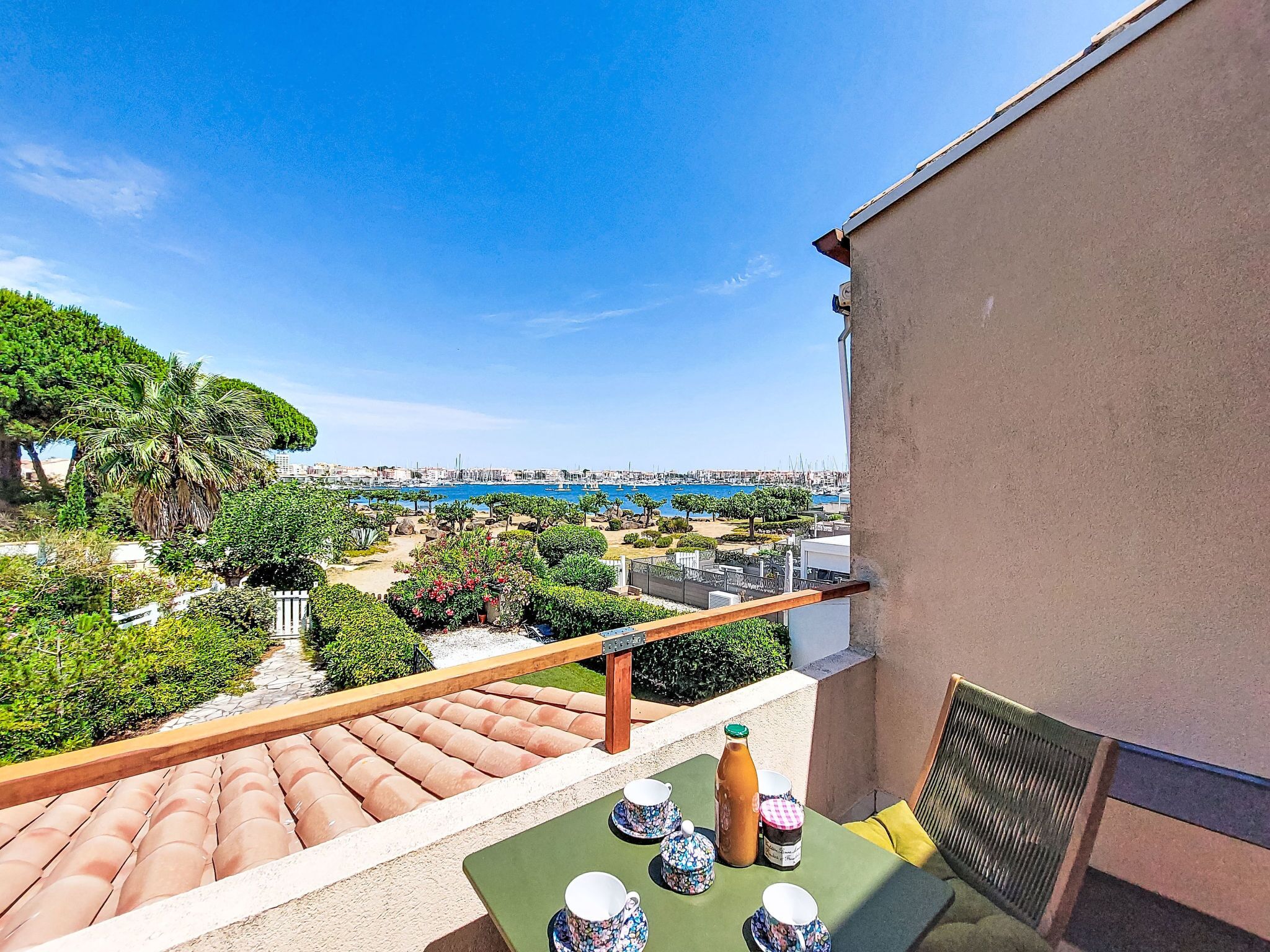 Varanda com mesa posta para o chá, com vista para um porto e para a paisagem urbana.