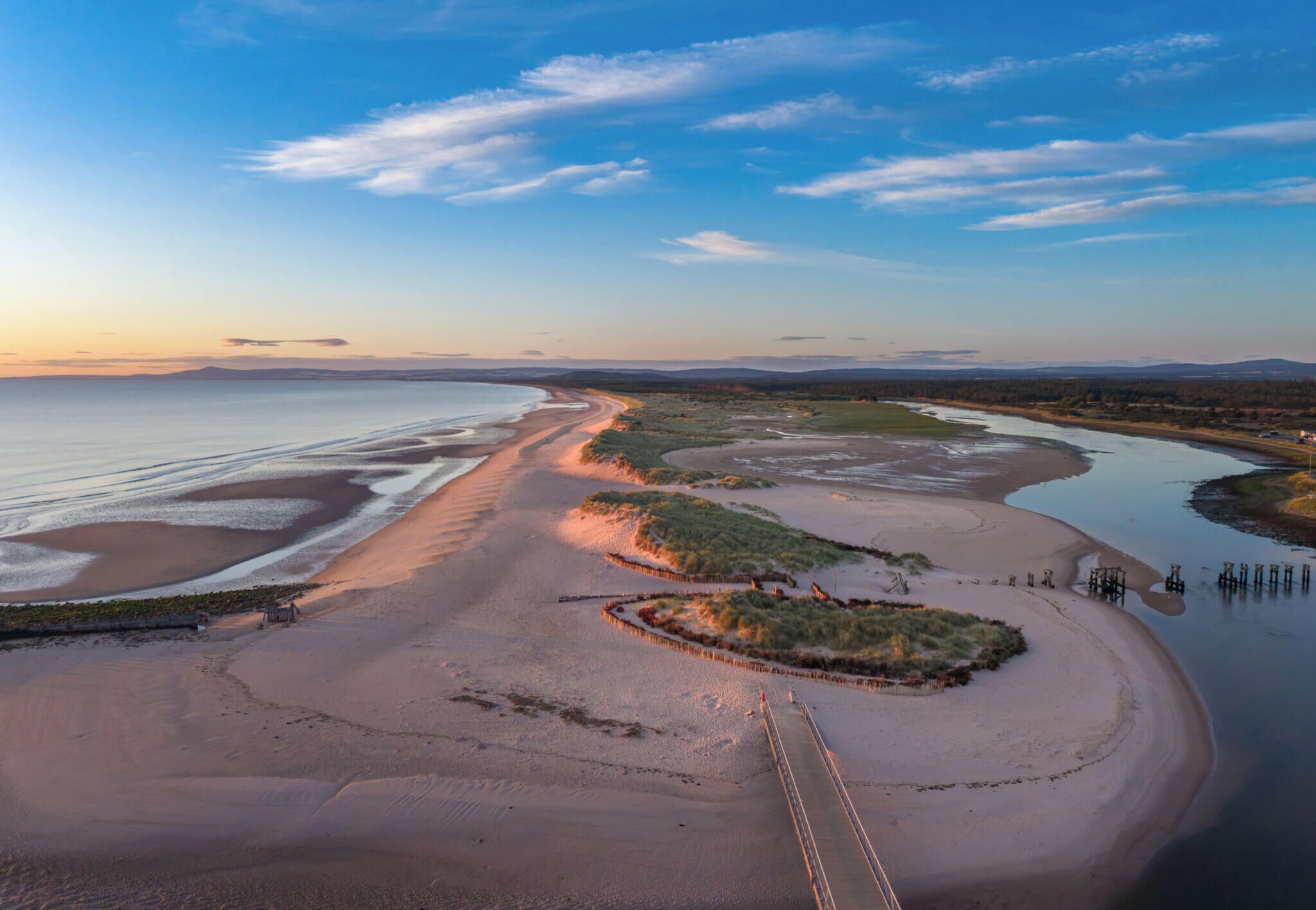 Un paysage côtier avec une plage de sable, une rivière et un pont.