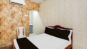 A hotel room with a bed, an air conditioning unit, a chair, and a bathroom visible through a door. - Classic Vishnu's Galaxy Rooms (Chennai)