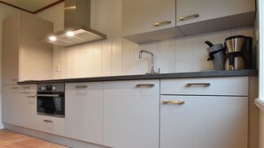 Moderni keittiö, jossa on valkoiset kaapit, ruostumattomasta teräksestä valmistettu uuni, kahvinkeitin ja pesuallas.