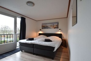 Ein Schlafzimmer mit einem Bett, einem Bild darüber und Blick durch ein großes Fenster.