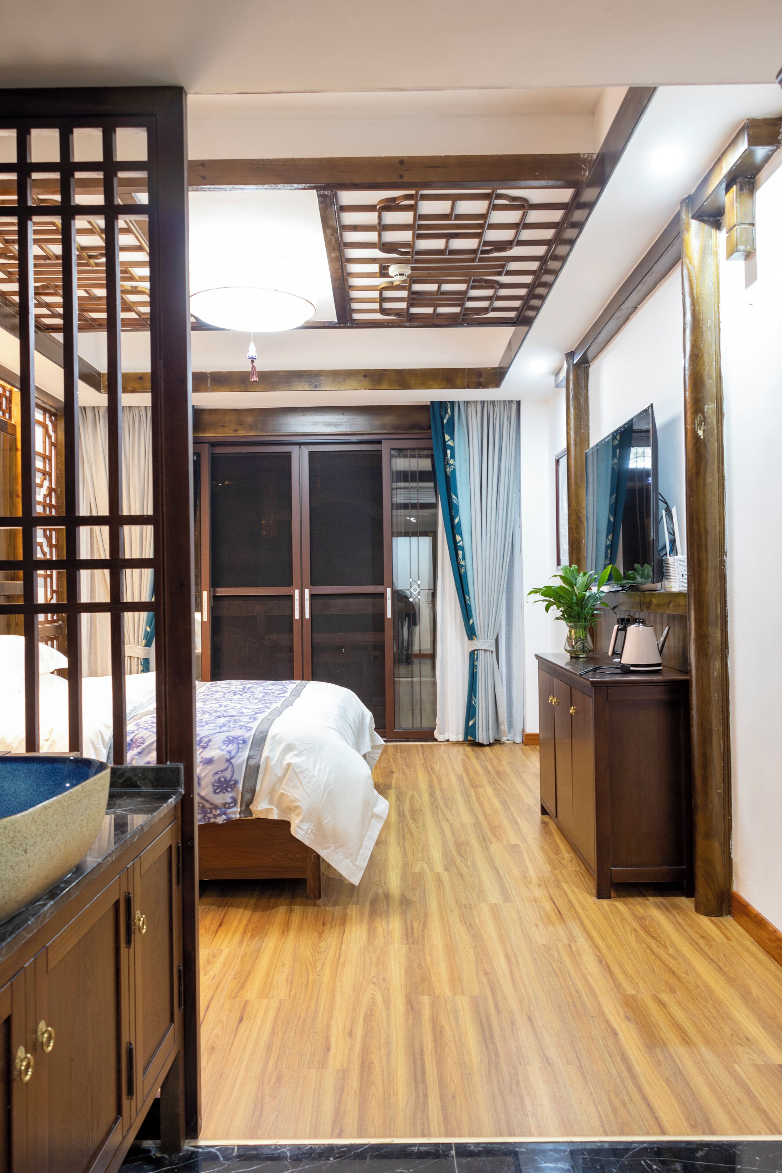 A hotel room with a bed, wooden flooring, a wardrobe, a desk with a lamp, and a mirror.