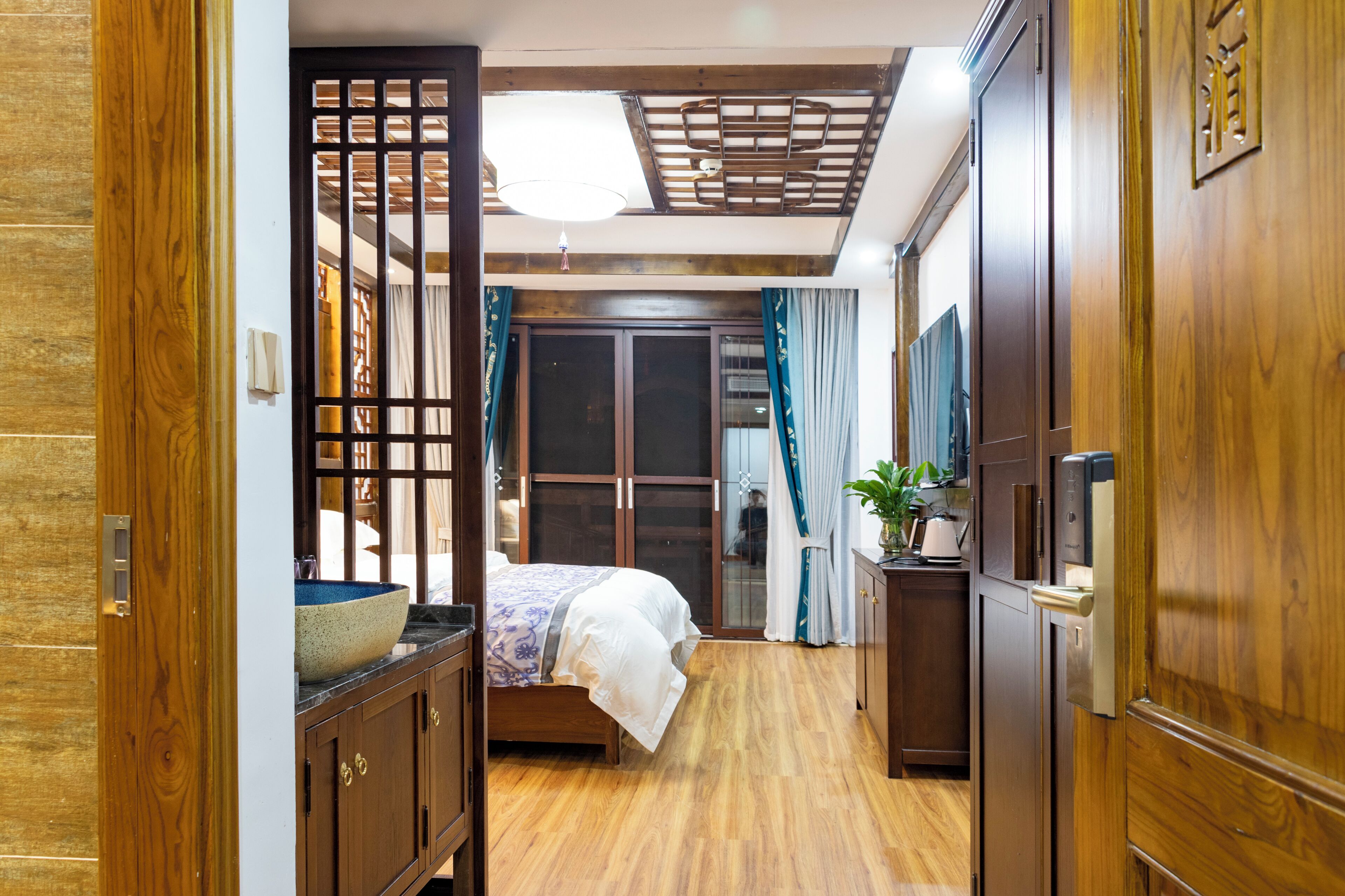 A bedroom with a bed, wooden wardrobe, and a small table with a plant.