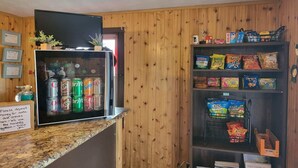 Un comptoir équipé d’un réfrigérateur pour boissons, d’étagères pour les en-cas et d’un panneau indiquant qu’il faut déposer de la monnaie pour les boissons gazeuses et les en-cas.