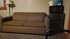 Un canapé marron, une chaise noire, une lampe et un four à micro-ondes sont posés sur un réfrigérateur noir dans une pièce aux murs de couleur beige.