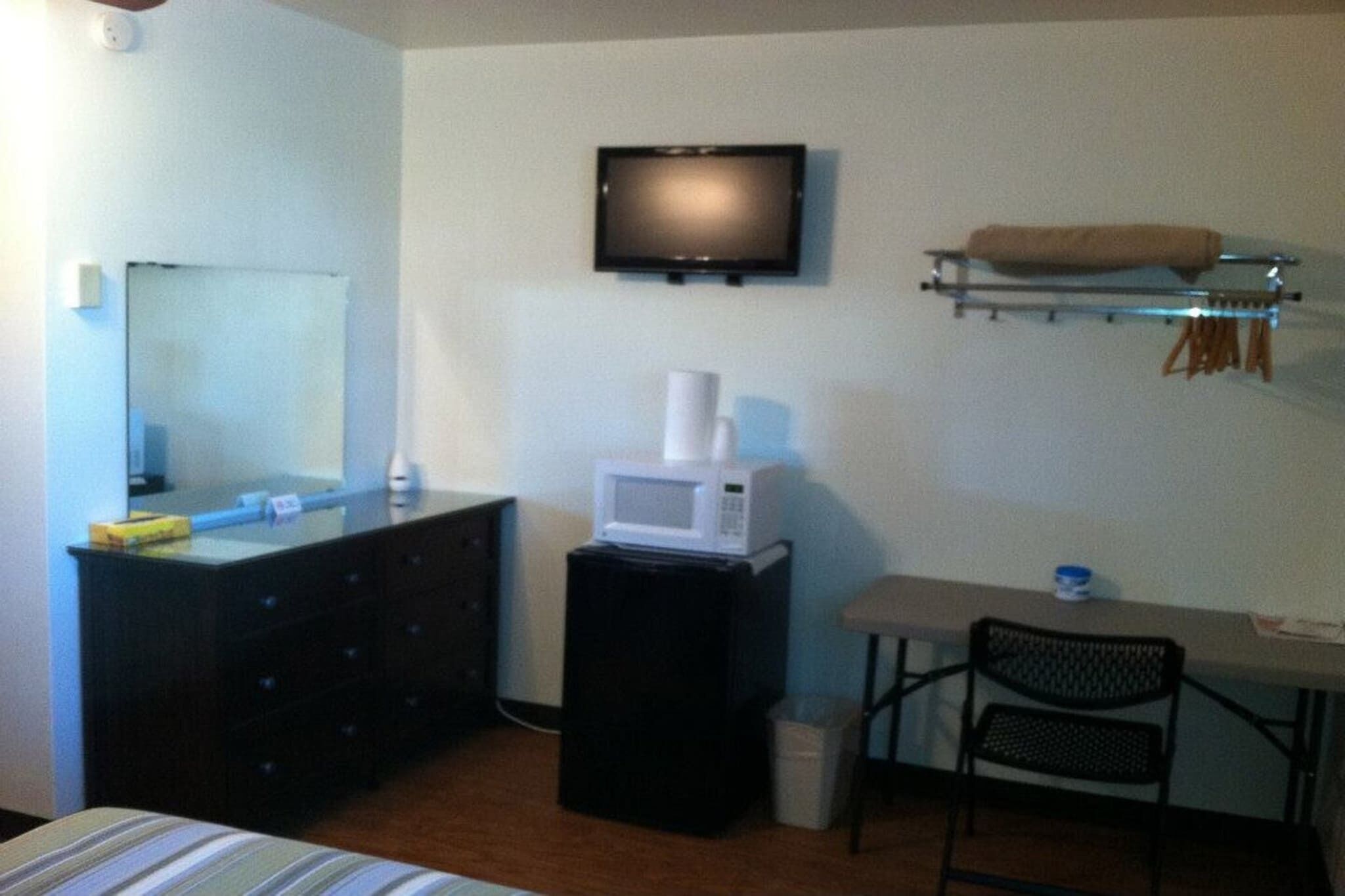 A hotel room with a bed, a dresser, a microwave, a television, a chair, and a small table.