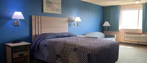 A hotel room with a bed, two bedside lamps, a nightstand, a window with curtains, and a wall-mounted picture.