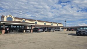 Un motel con zona de estacionamiento techada, varios vehículos aparcados y cielo despejado.