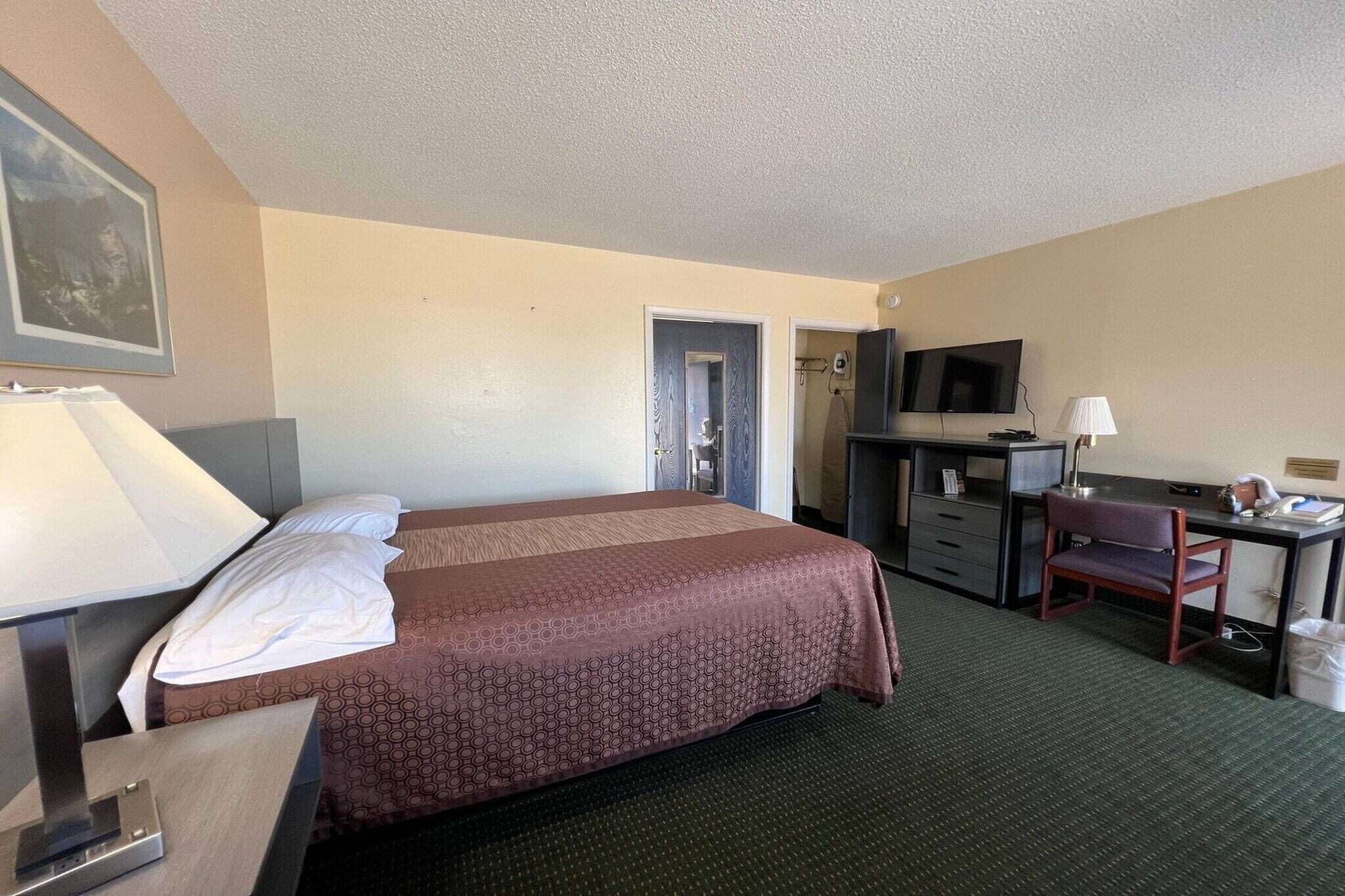 A hotel room with a bed, desk, chair, TV, and a door leading to another room.