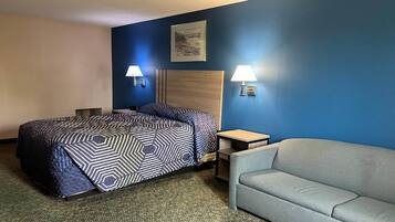 A hotel room with a bed, two bedside lamps, a gray sofa, and a framed picture on the wall.