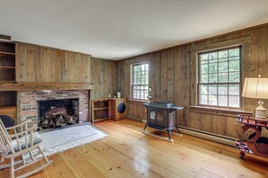 A room with wooden walls, a fireplace, a large window, and a wood-burning stove.
