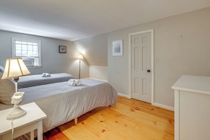 A bedroom with two beds, a bedside table with a lamp, a window, and a door.