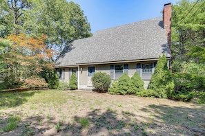 A two-story house with a sloped roof, surrounded by a variety of trees and shrubs.