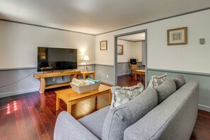 Una sala de estar con un sofá, un televisor, una mesa de centro de madera y una lámpara.