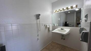 A bathroom with a white tiled wall, a sink, a mirror with lights, a hairdryer, and a hand dryer.
