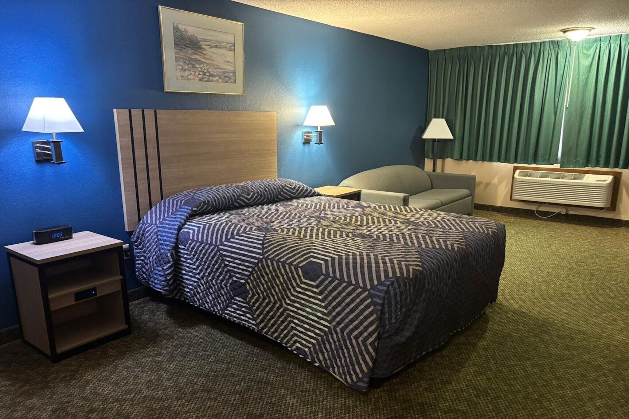 Habitació d'hotel amb un llit, dues làmpades de nit, una cadira, un escriptori i aire condicionat fixat a la paret.