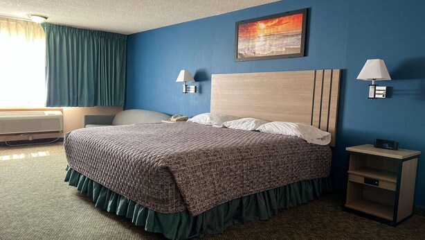 Una habitación de hotel con una cama, dos lámparas de noche, una mesita de noche, un cuadro y una ventana con cortinas.