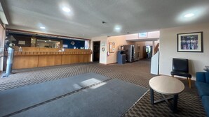 Un vestíbulo de hotel con una recepción, un área de espera con un sofá y una mesita, y un refrigerador.