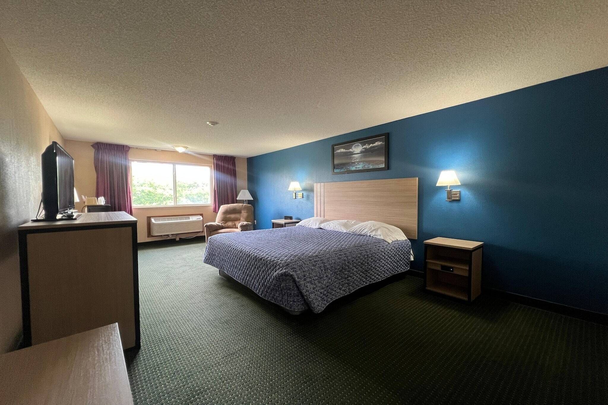 Una habitación de hotel con cama, escritorio, silla, dos lámparas de noche y ventana con cortinas.