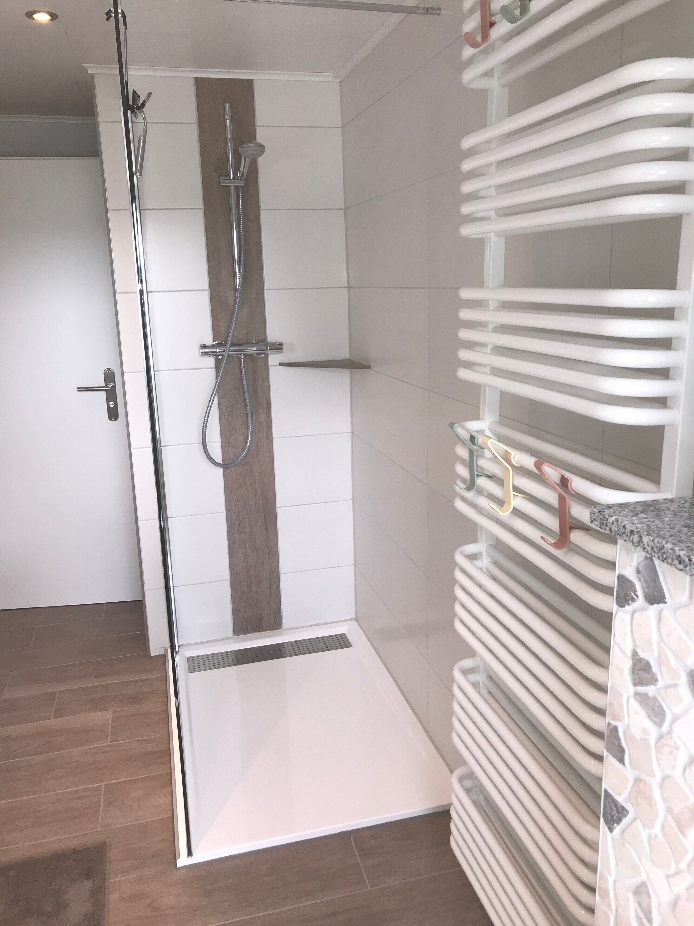 Een moderne badkamer met een douchecabine van glas, een houten accentmuur en een betegelde vloer.
