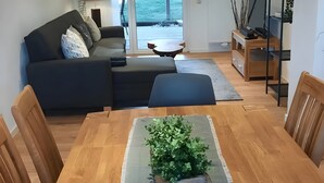 A modern living room with a sofa, a coffee table, a dining table with chairs, and a TV stand.
