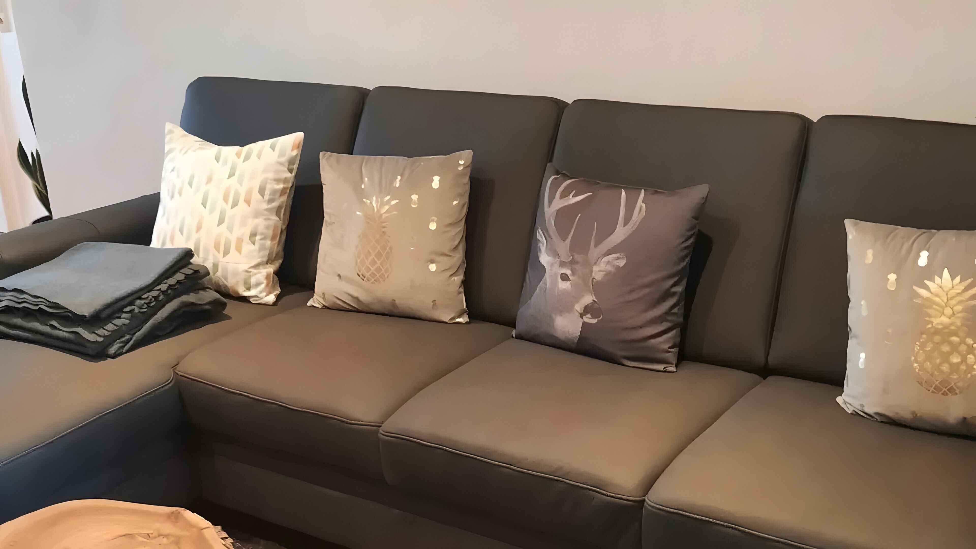 Un divano componibile con quattro cuscini, una coperta piegata e una borsa sul pavimento.