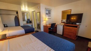 A hotel room with two beds, a desk, a television, a mirror, and a small refrigerator.