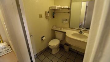 Et lille badeværelse med toilet, håndvask og spejl. Der er en bøjle over vasken og en skraldespand ved siden af toilettet.