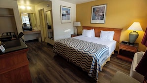 A hotel room with a bed, a desk, a chair, a mirror, and a lamp. - Queen Bed Accessible Non-Smoking (Pendleton OR)