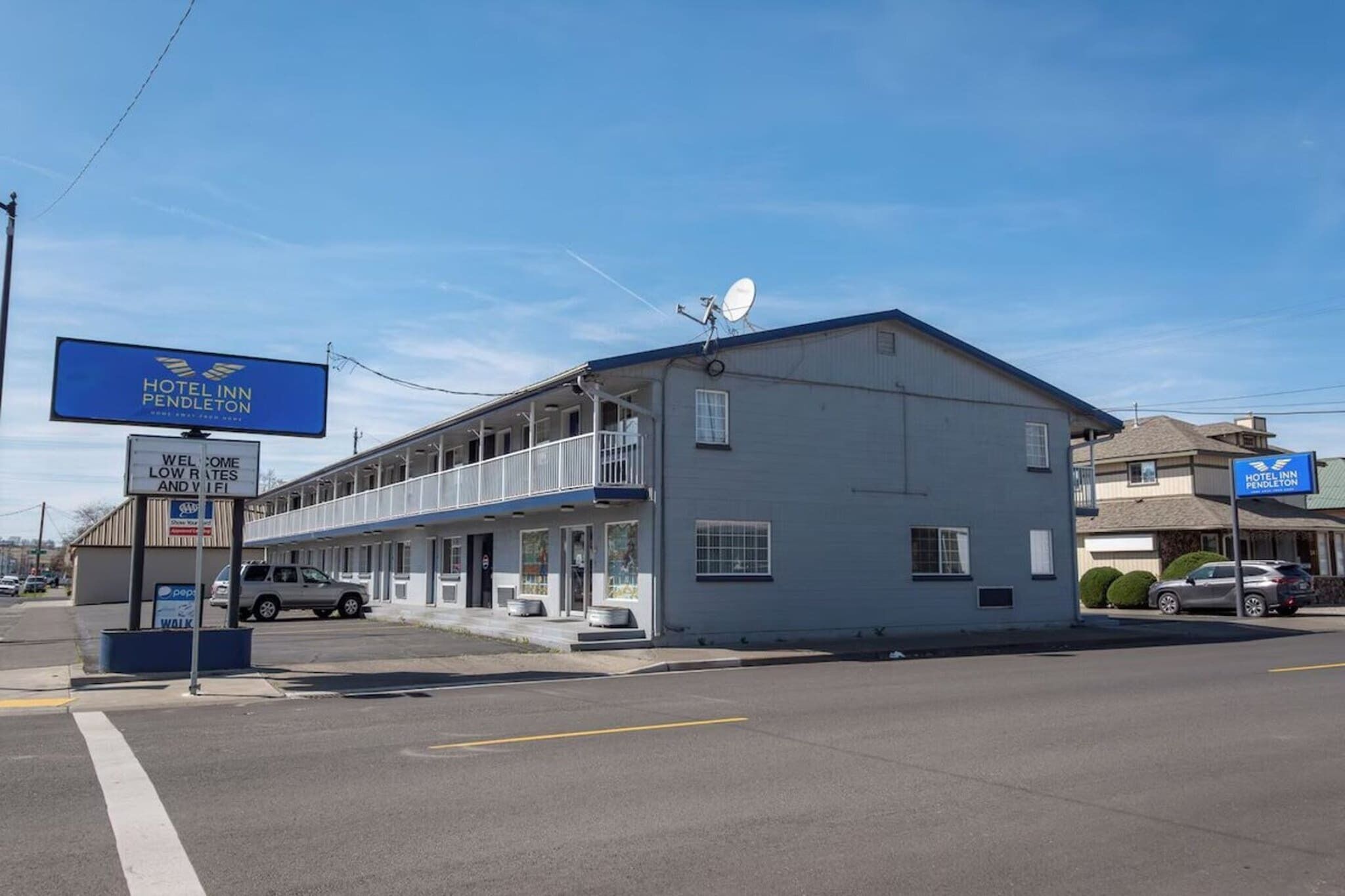 Un motel de dos pisos con un letrero, una antena parabólica y una entrada visible.