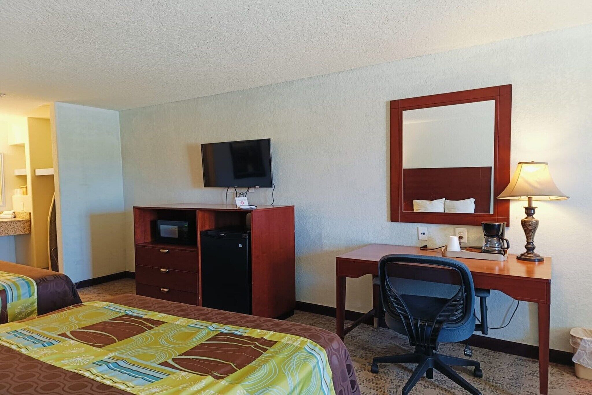 Habitación de hotel con dos camas, un escritorio, una silla, un televisor, un espejo, una lámpara y una cafetera.