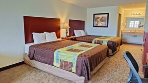 A hotel room with two beds, a nightstand, a lamp, a framed picture on the wall, and a bathroom with a sink and mirror.